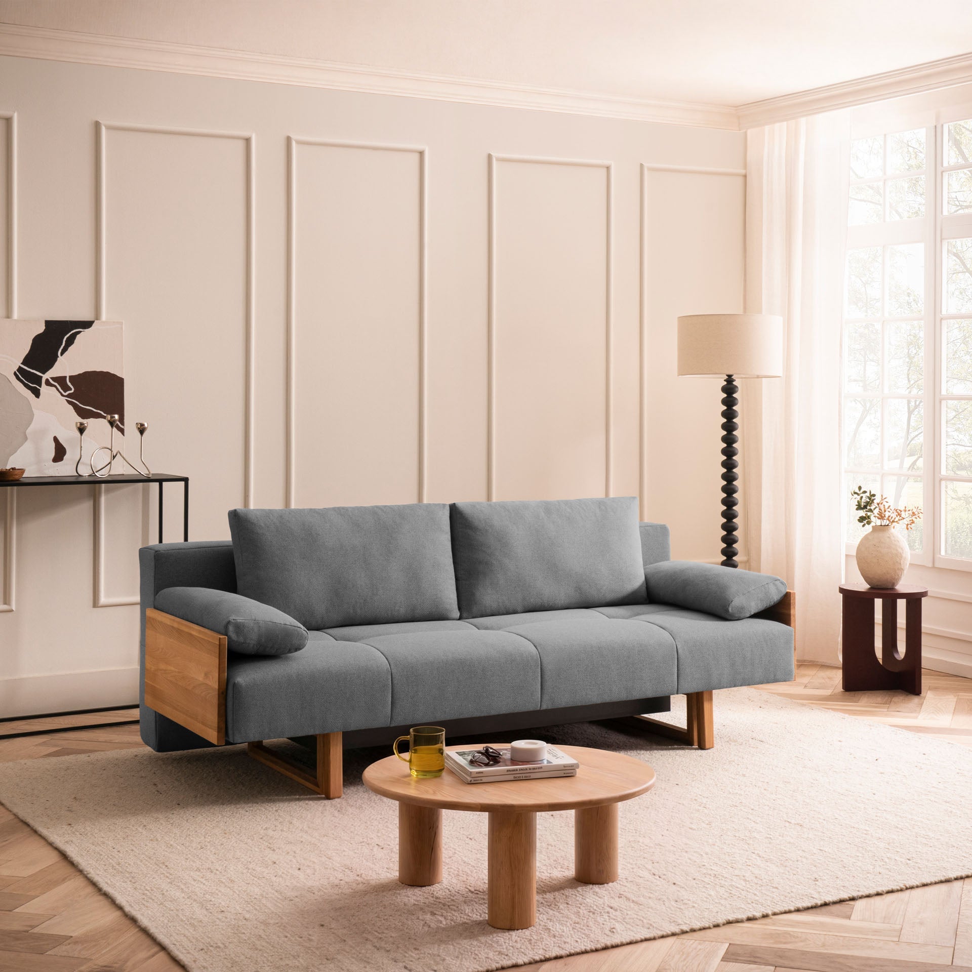 Sofa in Anthrazit mit sichtbaren Eichen-Armlehnen in modernem Wohnzimmer mit Stehlampe und rundem Holz-Beistelltisch