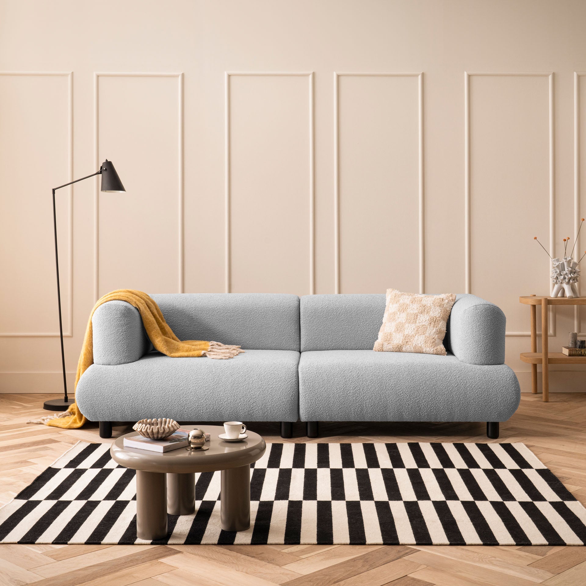 Modernes graues Sofa mit weicher Polsterung, Kissen und gelber Decke im hellen Wohnzimmer mit Teppich und Beistelltisch